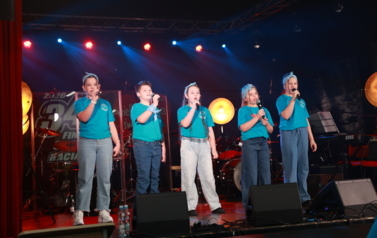 sześcioro dzieci w wieku szkolnym śpiewa na scenie 