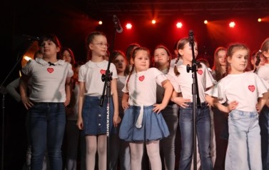 Grupa dzieci w wieku szkolnym śpiewa na scenie 