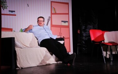 aktor na scenie - siedzi na sofie 