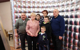 Dziadkowie i babcie pozują z wnuczkami na tle srebrnej ścianki. 